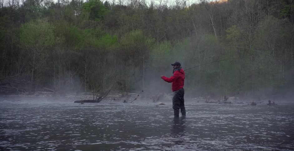 Bearded man fly fishing in a river on a very overcast and misty day