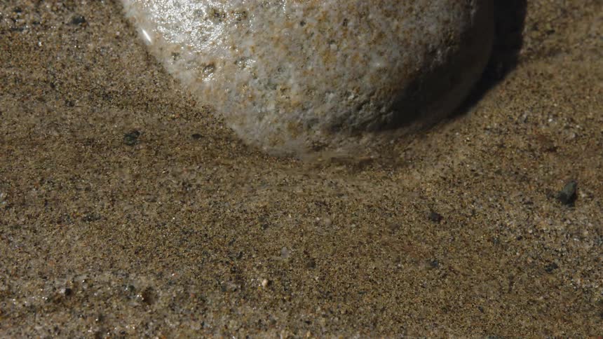 Water flowing on the sand next to a rock