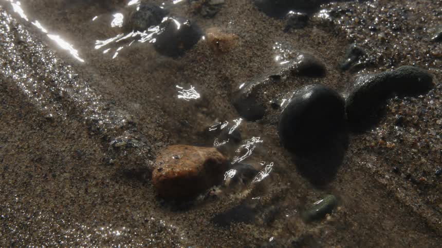 Close up of sand with small stones and flowing water