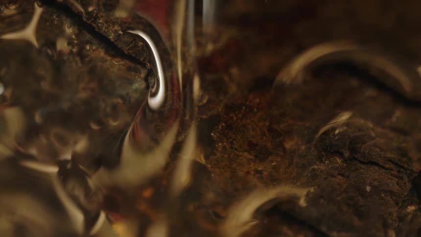 Transparent amber fluid flows across a rough brown surface