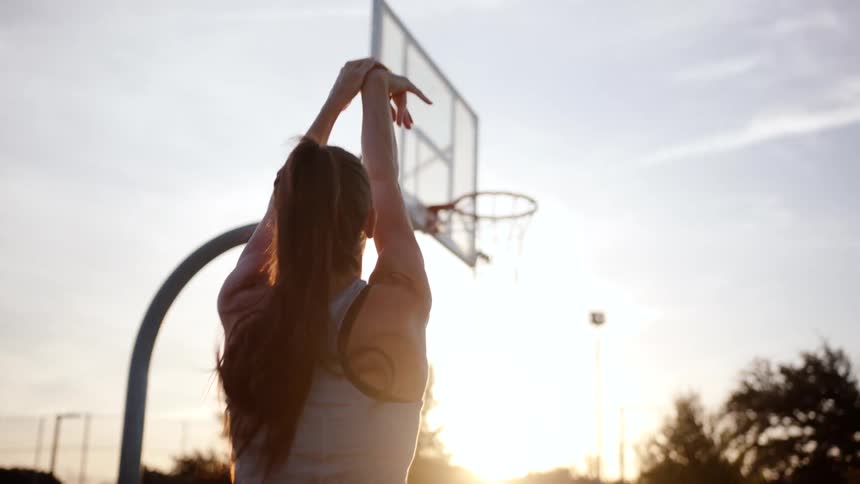 Woman playing basketball on a court in the late afternoon