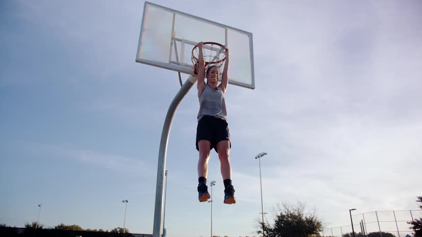 Woman leaning on the hoop of a basketball court