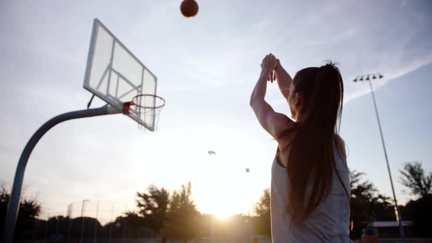 Woman on a basketball court shooting the ball into the basket in the late afternoon