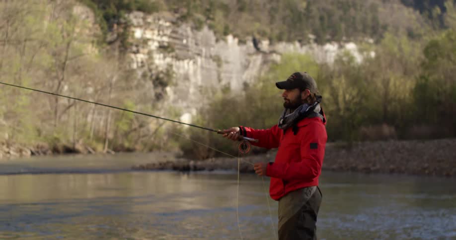 A man that is next to a pond and he is fly fishing