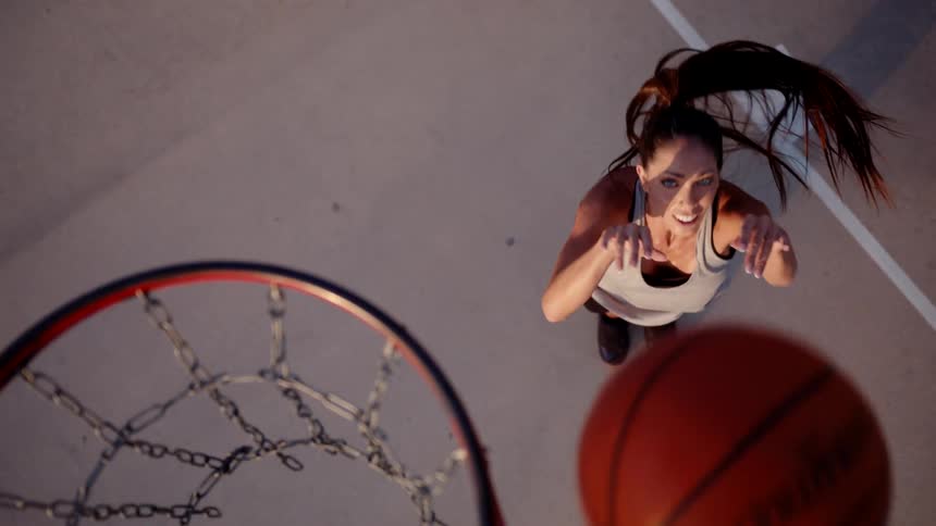 Top view of a woman jumping and throwing a basketball into the hoop