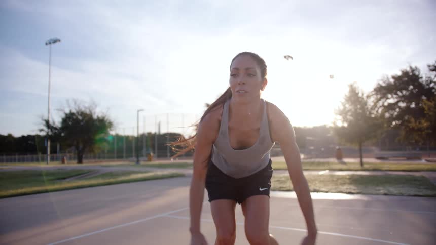 A young woman is bouncing a basketball on the ground and then throwing it up