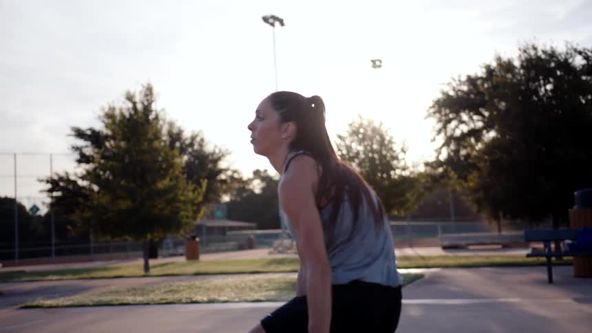 A woman in athletic wear dribbles a basketball on the court heading towards the net and taking a shot