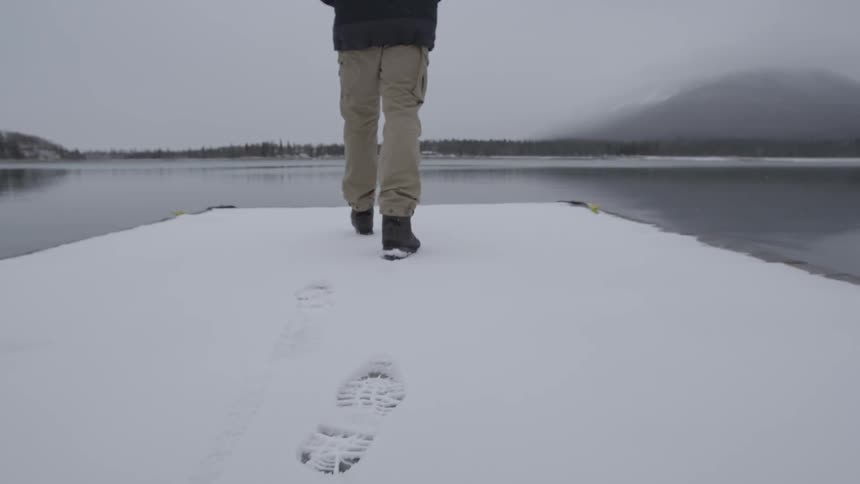 A man walks on a snow covered dock towards the water