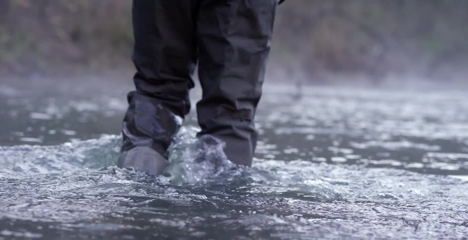 Fly fisher wading through some water as seen from the waist down