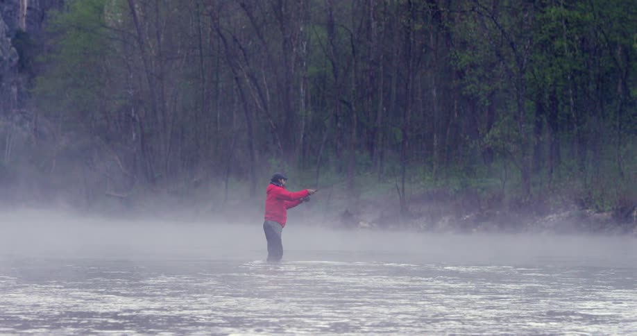 A fisherman stands in a river and casts a fishing line