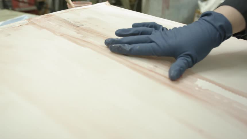 A person wearing rubber gloves runs their hand along the seam of a board