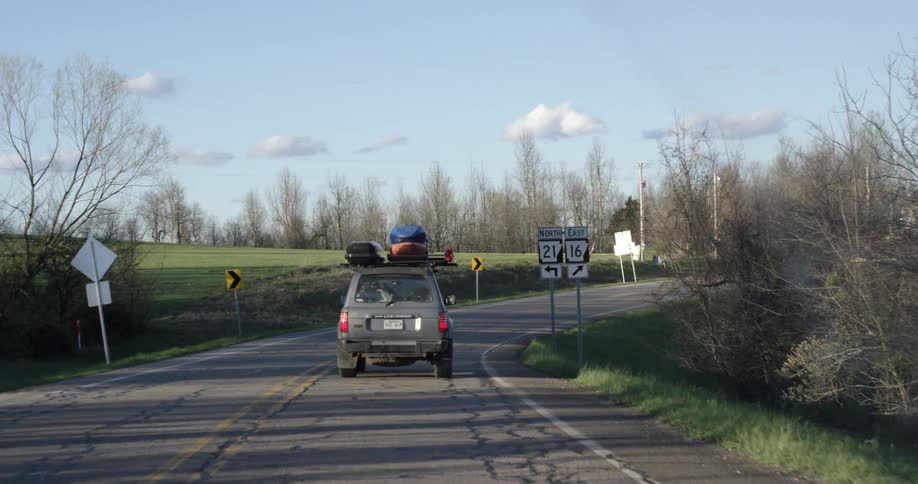 Vehicle driving down a paved road with a lot of equipment strapped to its top