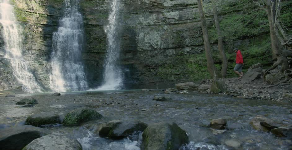 Man walking alongside a river to look at a waterfall