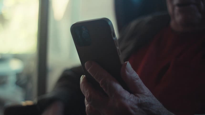 An elderly man talks on his smartphone while sitting indoors