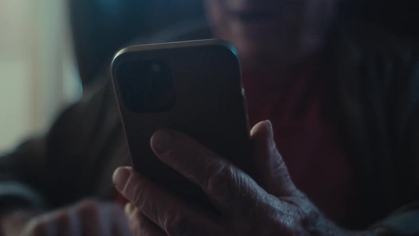 An old man smiles while talking to someone through a smartphone