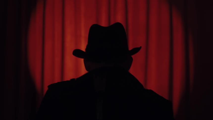 Silhouette of a man in a hat against a red curtain