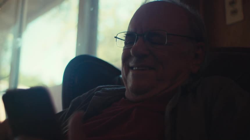 Elderly man smiles while scrolling on his smartphone at home