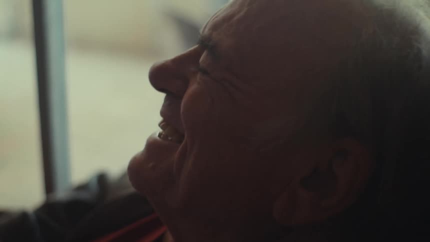 An old man sits in a living room and laughs