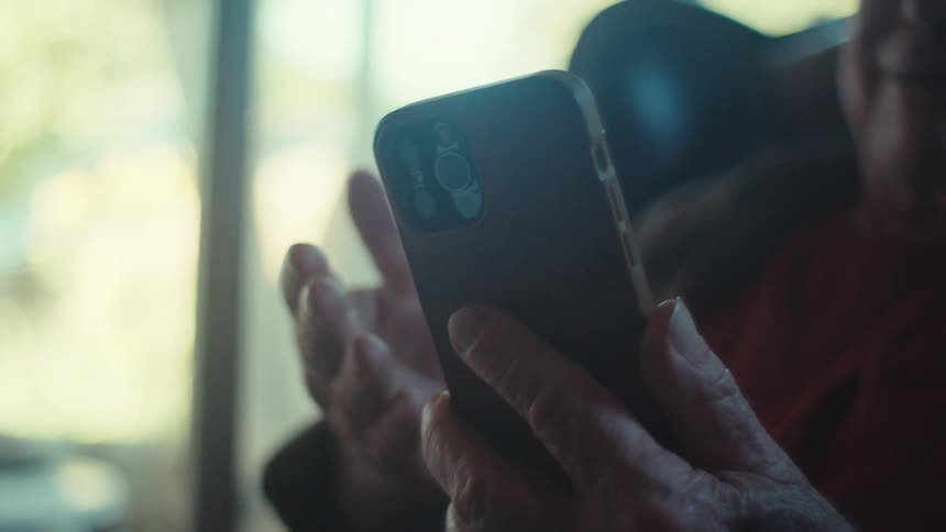 Elderly man sitting in an armchair interacting with an iphone