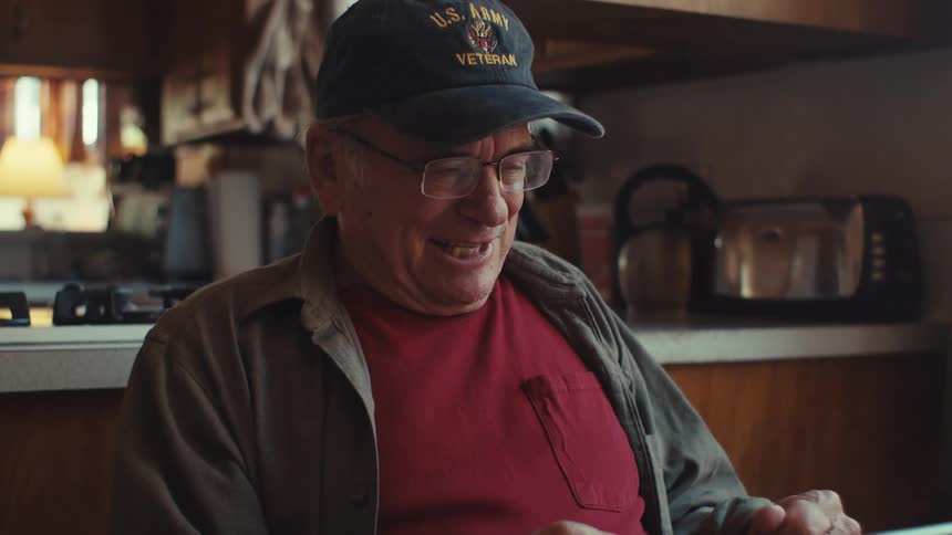 Elderly man sitting at a table interacting with a tablet with a happy facial expression