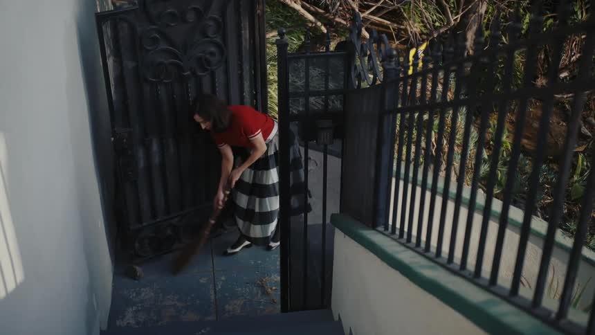 Woman sweeps the area at the base of the outdoor staircase leading to a metal gate