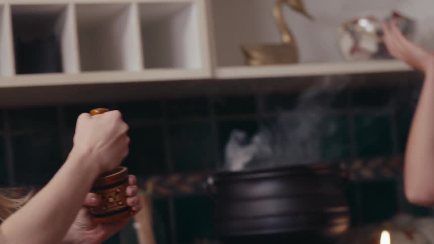 One friend balances a lid on her head and smells the vapor coming out of a pot while another uses a grinder during a get together