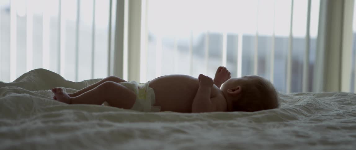 A baby lying on a bed by a window