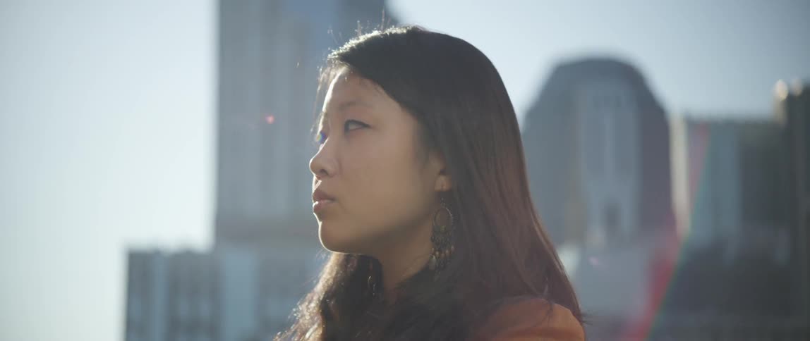 An asian woman looking around with part of a city skyline behind  her