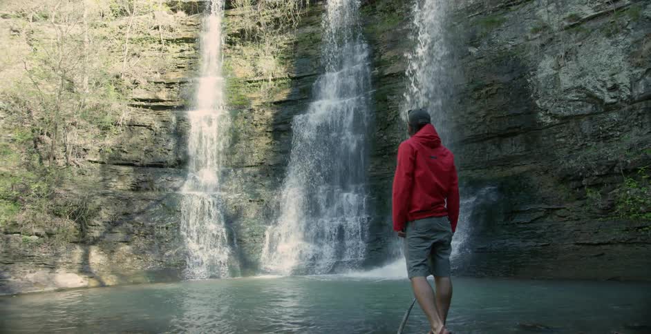 Man walking alongside a river to look at a waterfall