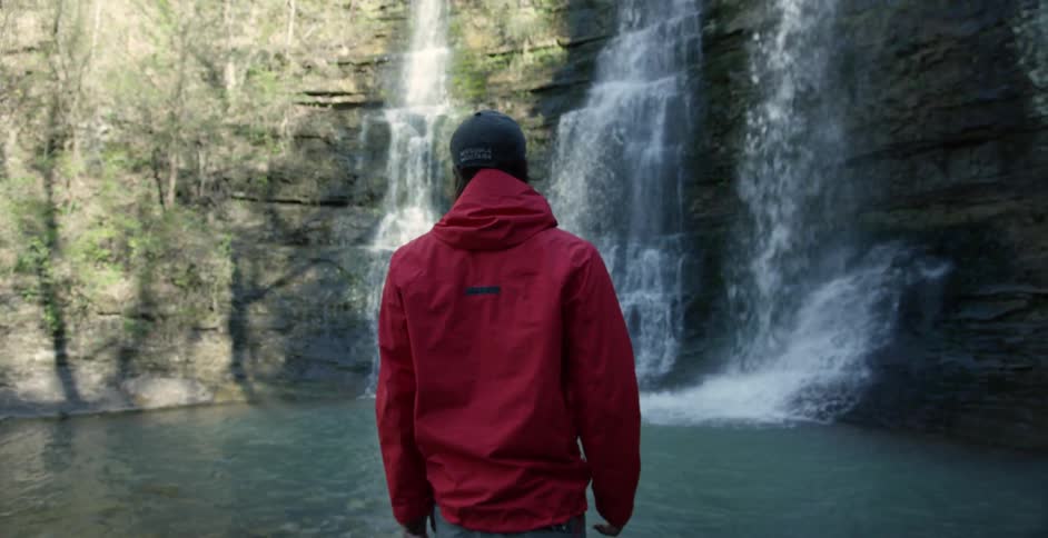 Man standing at the basin of waterfalls and looking up at them