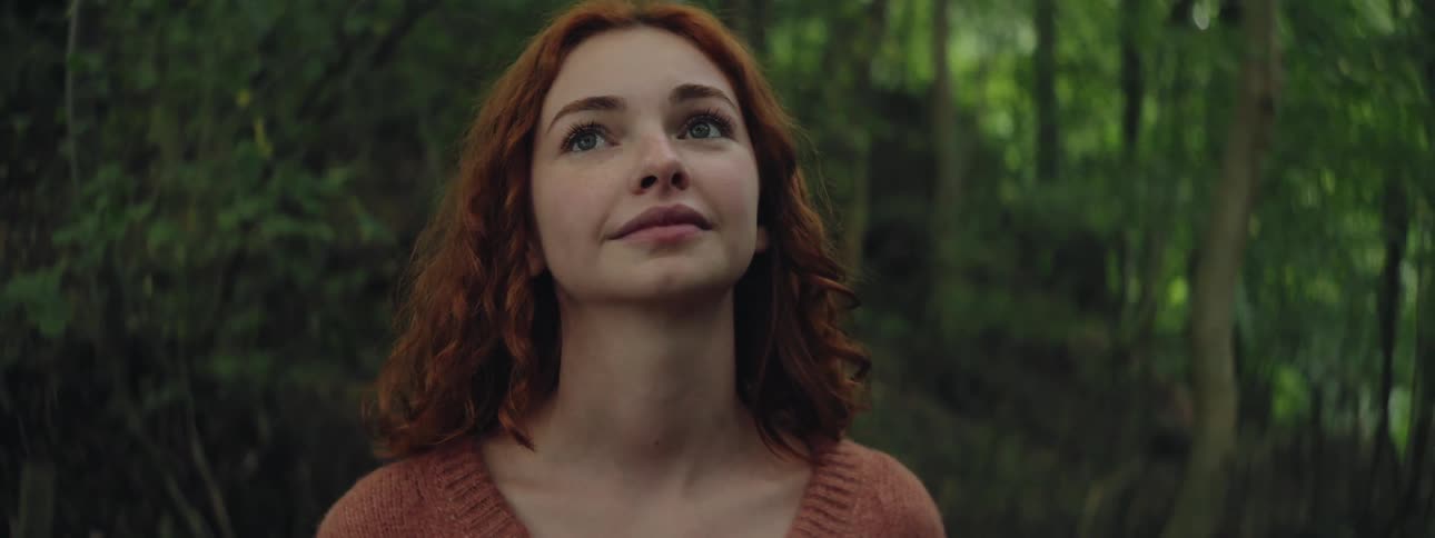 Portrait of a young redhaired woman looking up while standing in an environment surrounded by trees