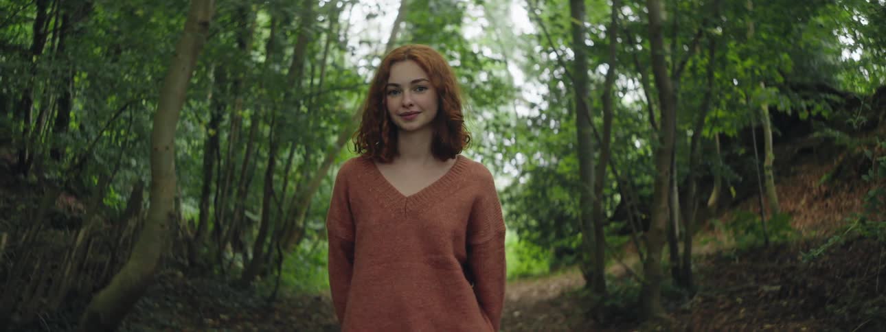 Teenage girl in a sweater stands in front of a forest