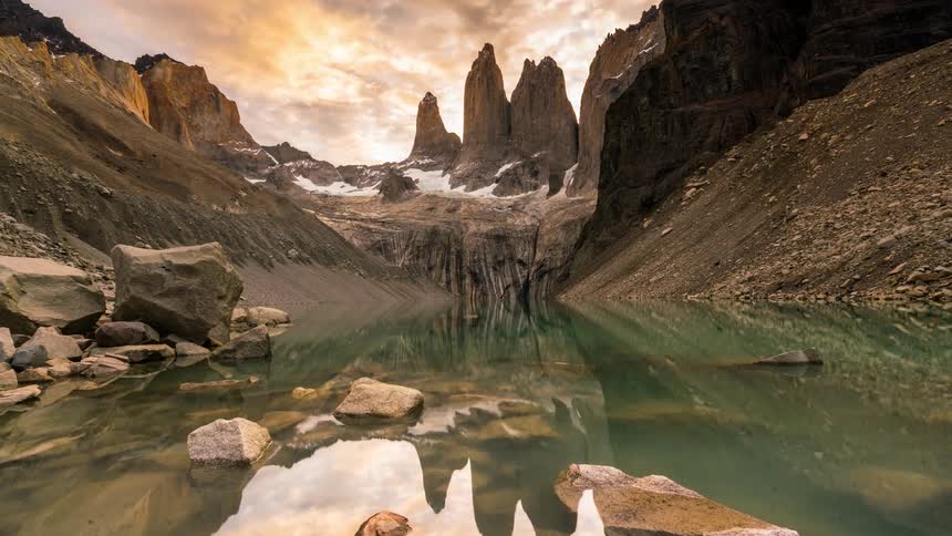 Natural landscape of a lake surrounded by snowy mountains and the darkening sky changing from orange to purple