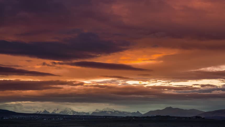 A rural environment with mountains in the background and an orange sky with several clouds passing by and it is getting dark