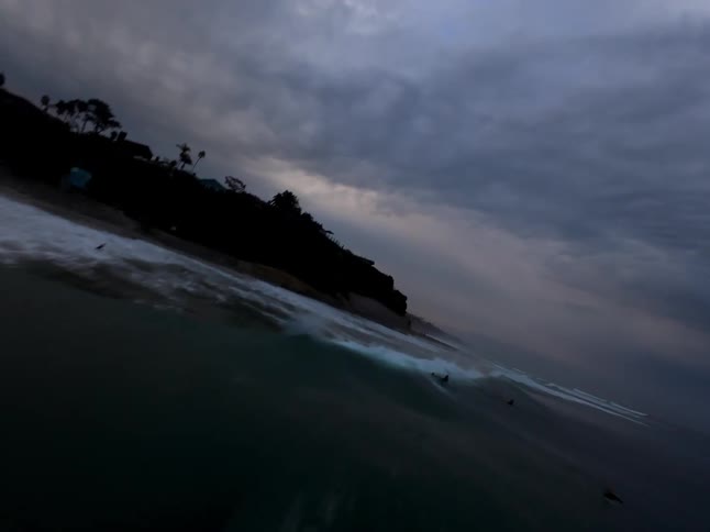 Aerial view of a dark stormy sky over a beach with surfers riding waves in the foreground
