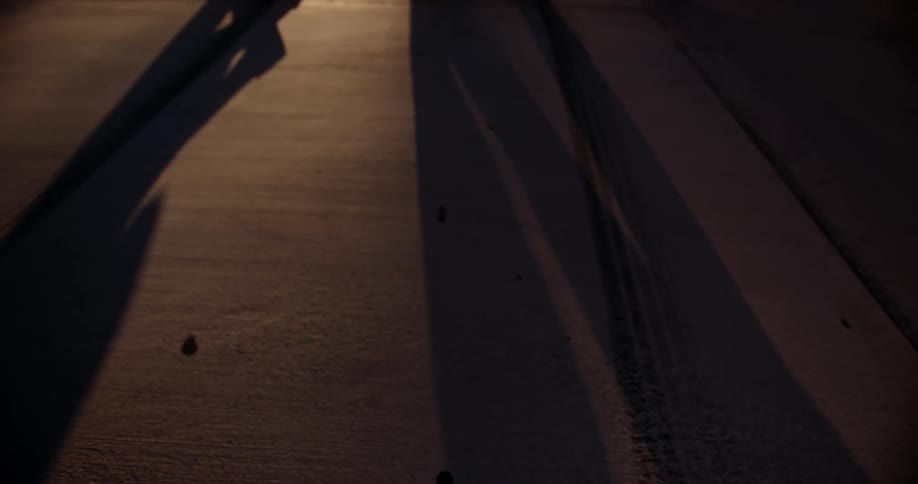 Two people casting shadows walk across a street at night