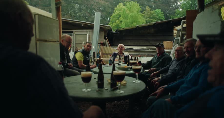 Several elderly men are sitting around a table that is full of bottles and glasses of beer