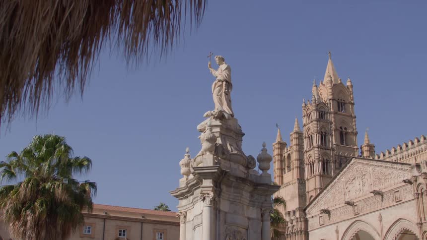 A statue of a woman holding a torch in front of a historic cathedral with intricate details and a clear blue sky in the background