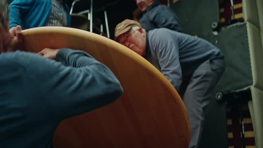 Four old men wrestle a wooden table top into a trailer