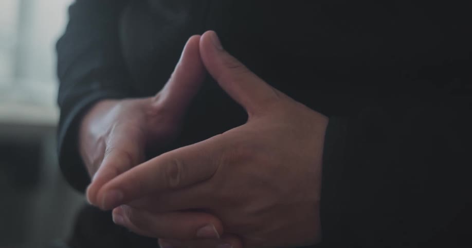A man in a black shirt holding his hands together with the thumbs and forefingers touching