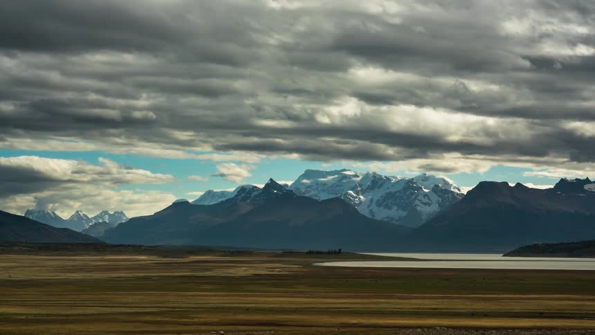 Natural landscape of a dog with a lake and snowy mountains in the background on a cloudy day