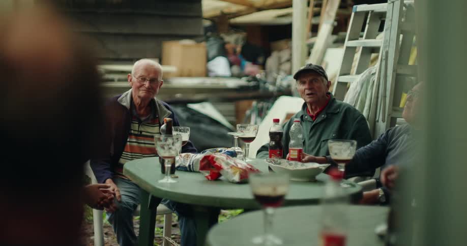 Group of men sitting at a table in an outdoor area with food and drinks talking to each other