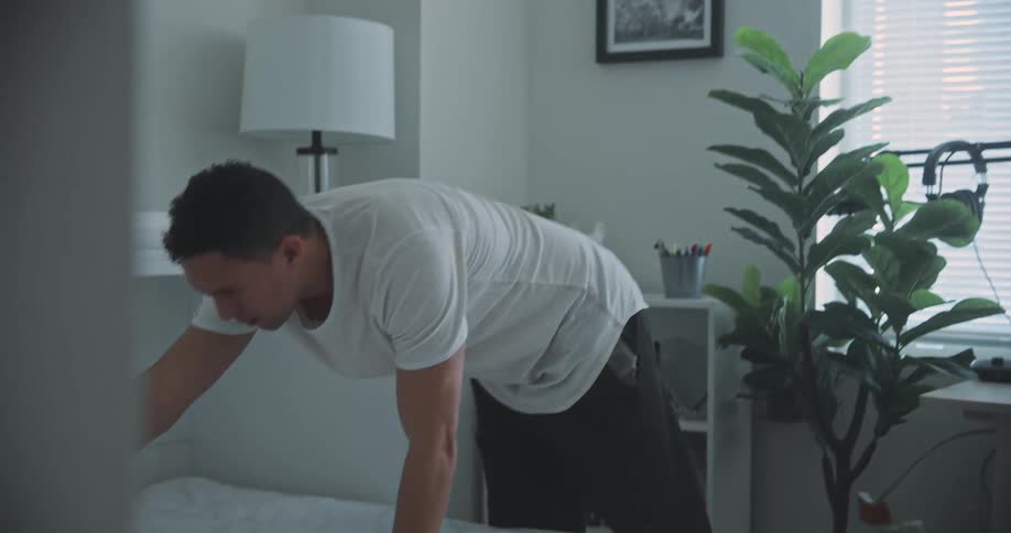 A man is cleaning his bed and throwing the pillows and bedding forward