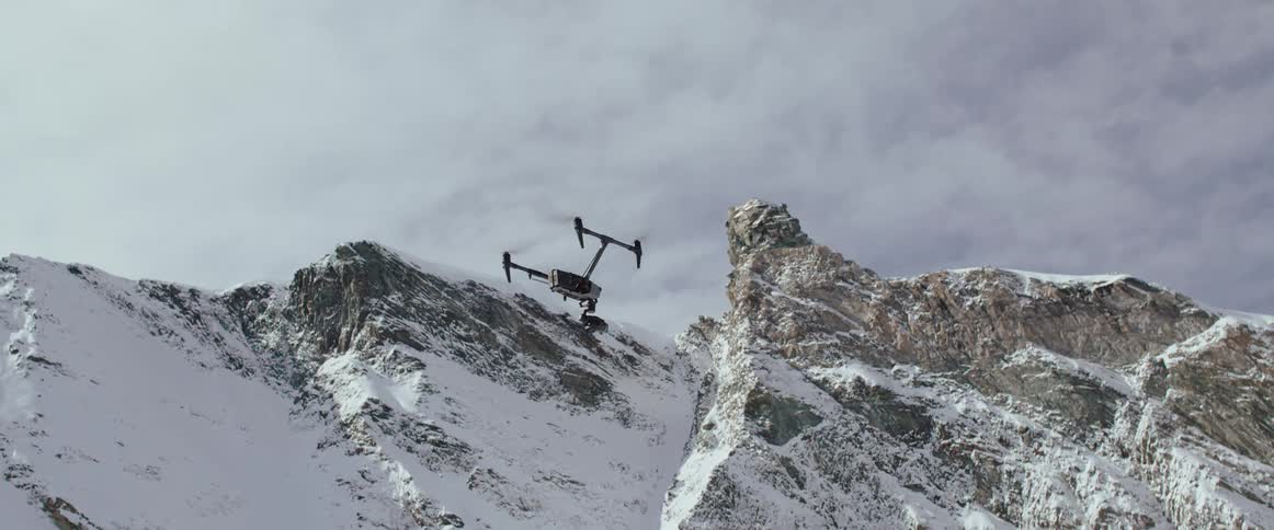 A drone gently flies next to a snowy arctic mountain