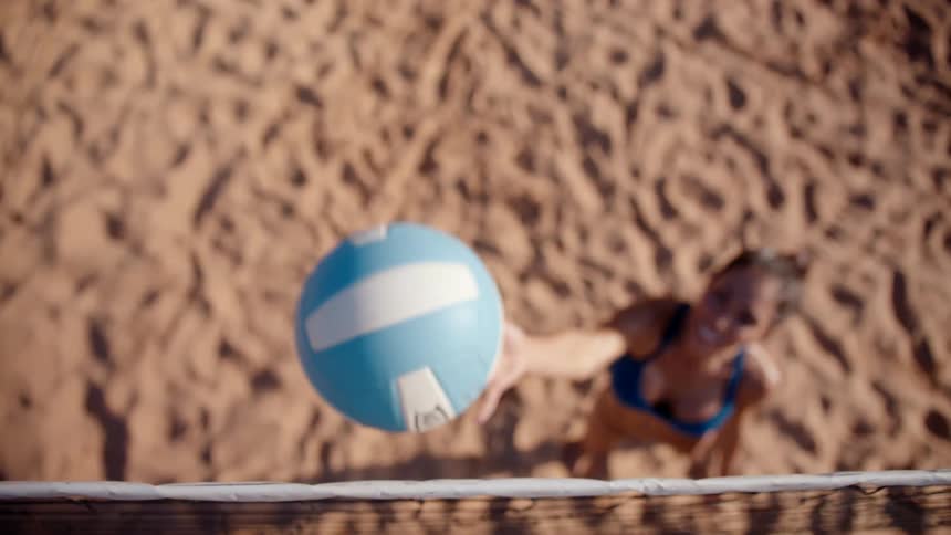 A female player standing on a sand court during a beach volleyball game throws the ball up