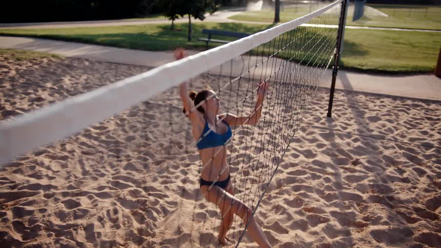 Woman jumping on a sand court and hitting a volleyball