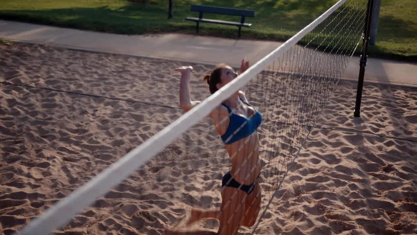Woman jumping on an open sand court and hitting a volleyball