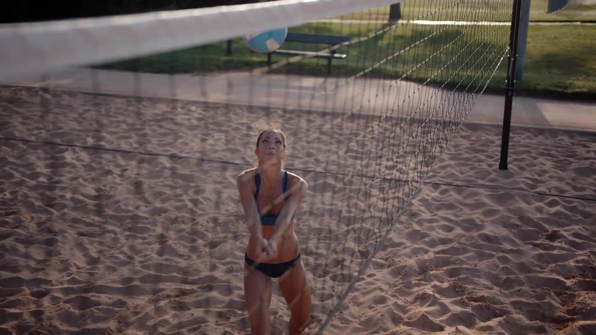 Woman hitting a volleyball upwards while standing on an open sand court
