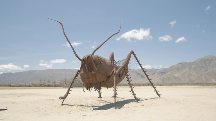 A grasshopper statue stands in a dirt field
