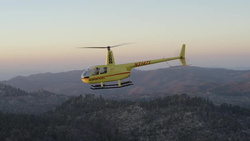 A yellow helicopter being filmed on the side in the air